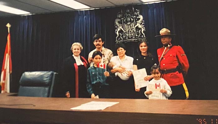 The Alvarez family at a law court posing for a picture as they receive their citizenship. From left to right, a judge, Mauricio, Mauricio jr, Flor holding baby Karen, Bonnie, Ivonne, and a Canadian Mountie.