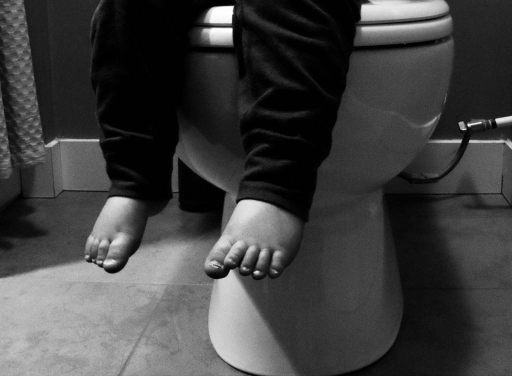Baby's feet as they hang off of a toilet. 