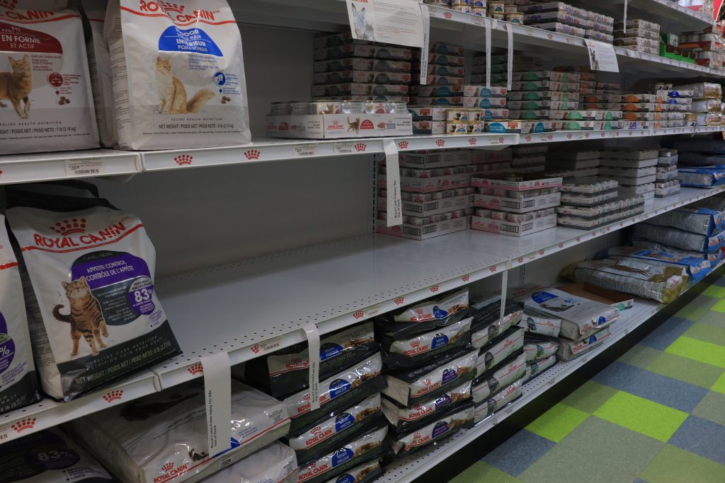 A shelf that contains multiple different kinds of pet food. Due to supply issues, gaps are visible where stock would normally be.