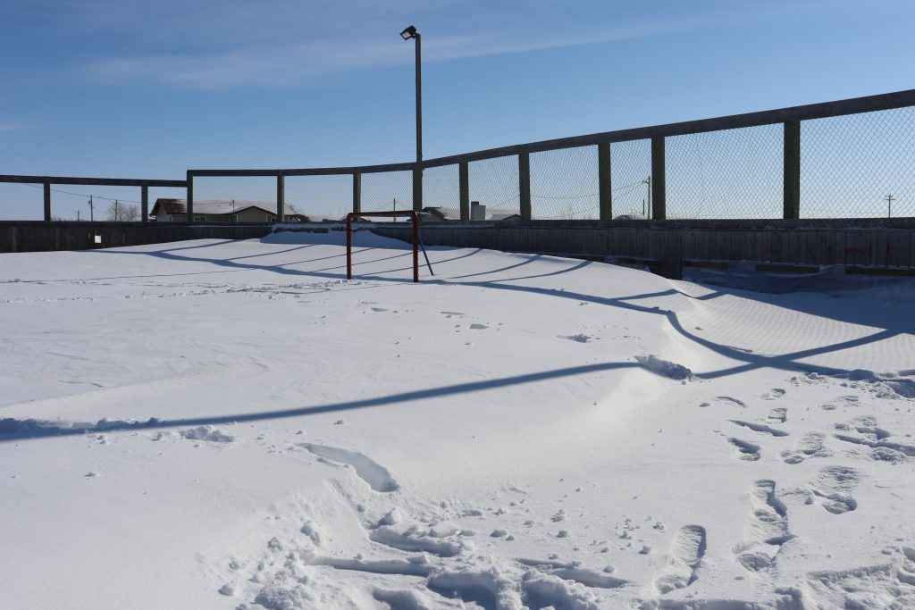 An outdoor hockey rink covered in a large amount of snow during the day.