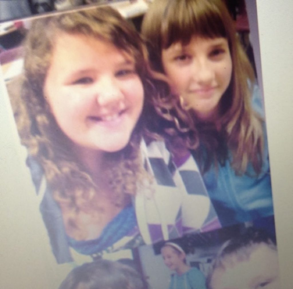 Two pre-teen girls posing for a photo in a school class room. 