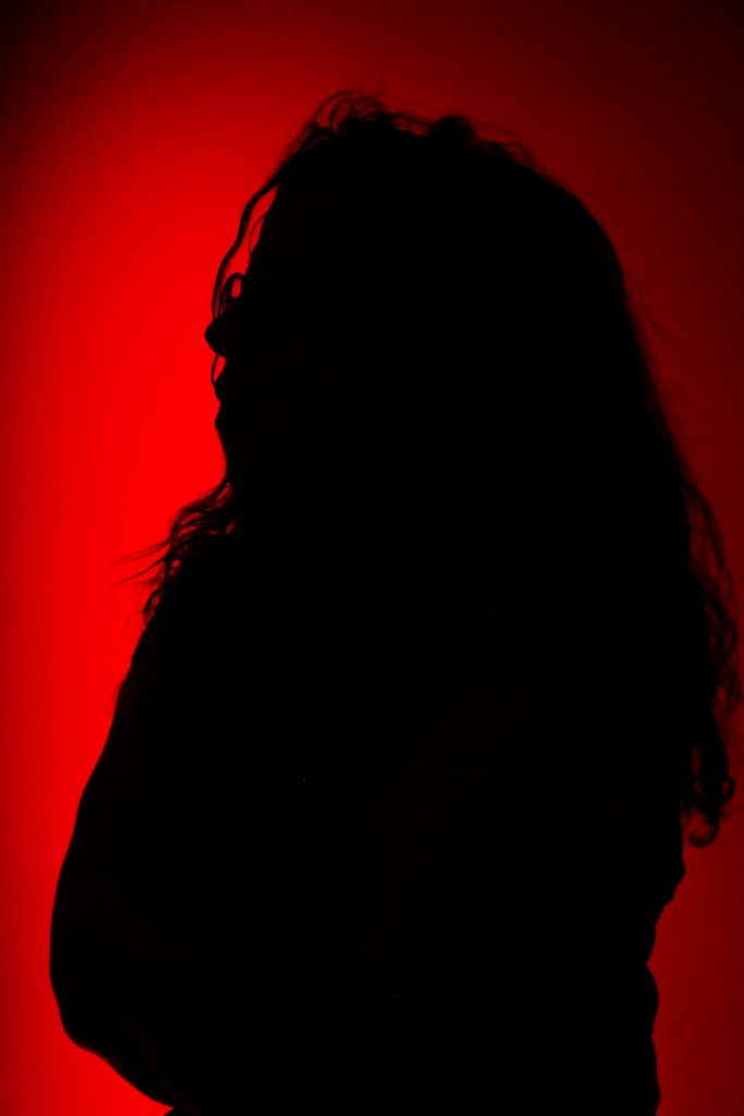 A woman with long wavy hair is silhouetted  on a red background. 