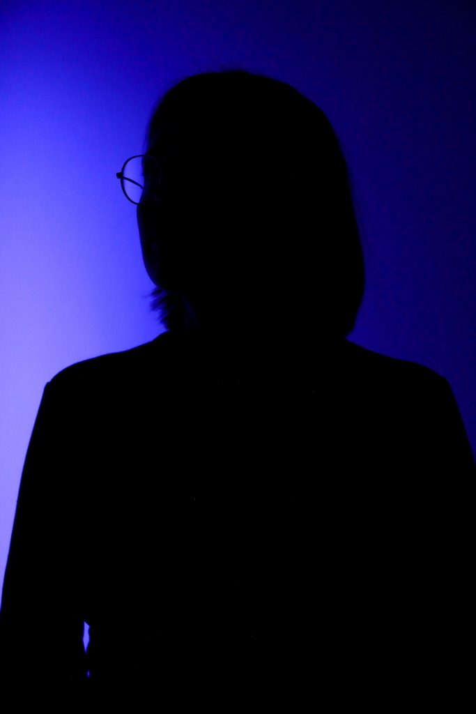 A woman in glasses is silhouetted on a blue background.