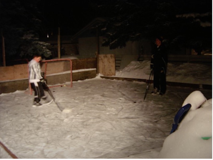 A young boy skates on an outdoor hockey rink at night.