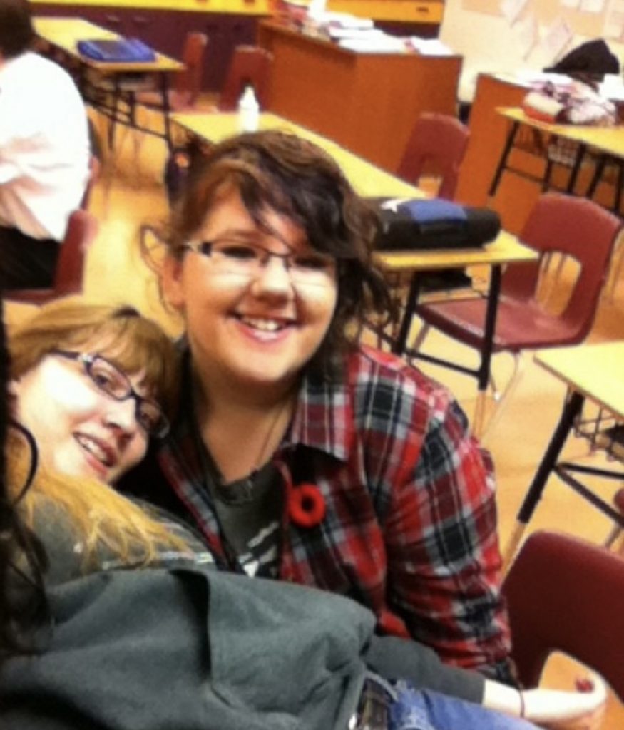 Two teen girls take a selfie together while sitting in a school class room