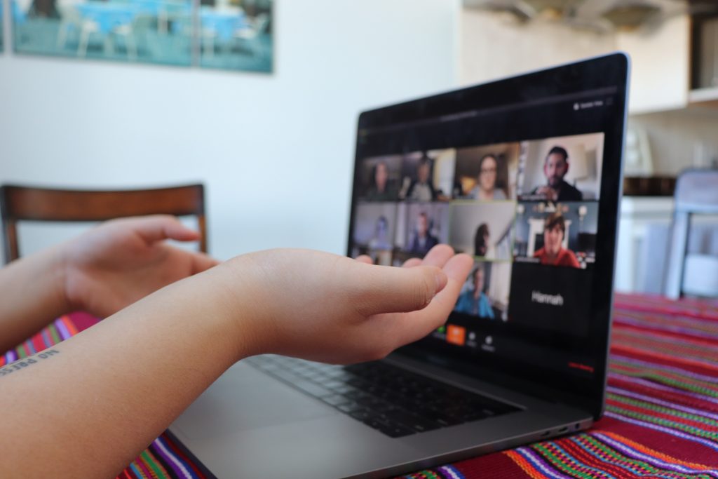 A photo of a woman's hands in front of a computer screen displaying a virtual meeting. 
